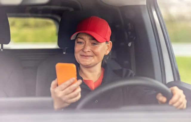 Woman sitting in her stationary car, smiling at her phone, using the Circle K app