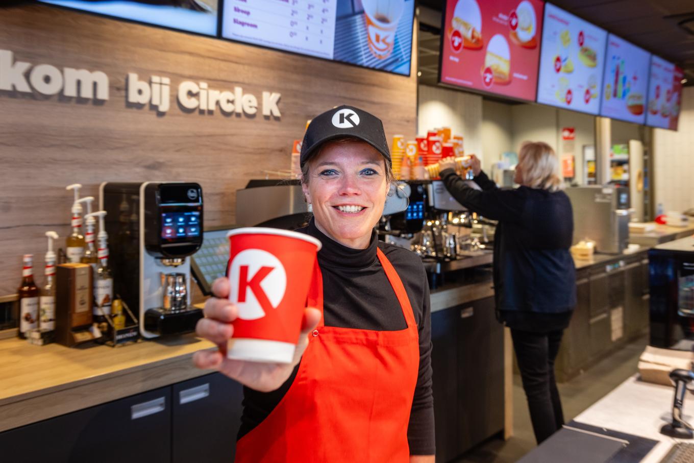 Medewerker van Circle K in de winkel met een beker in de hand
