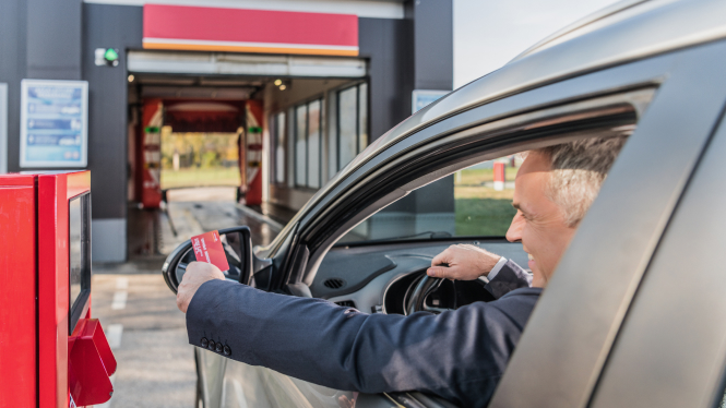 Persoon hangt uit het autoraam om te betalen voor de wasstraat