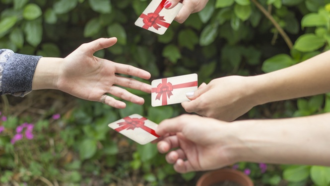 Ingezoomde foto van handen die cadeaubonnen aanreiken aan een uitgestoken lege hand